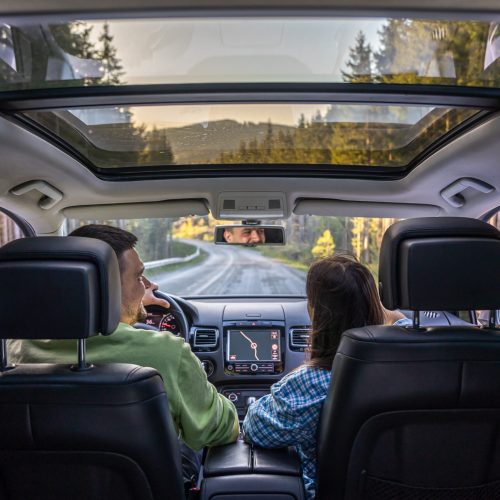 Back view of man and woman traveling in car. Beautiful young couple sitting on front passenger seats, man driving comfortable automobile.